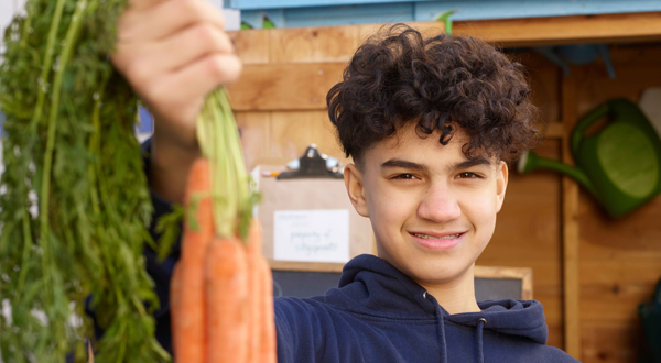 A boy holding carrots up in his right hand.