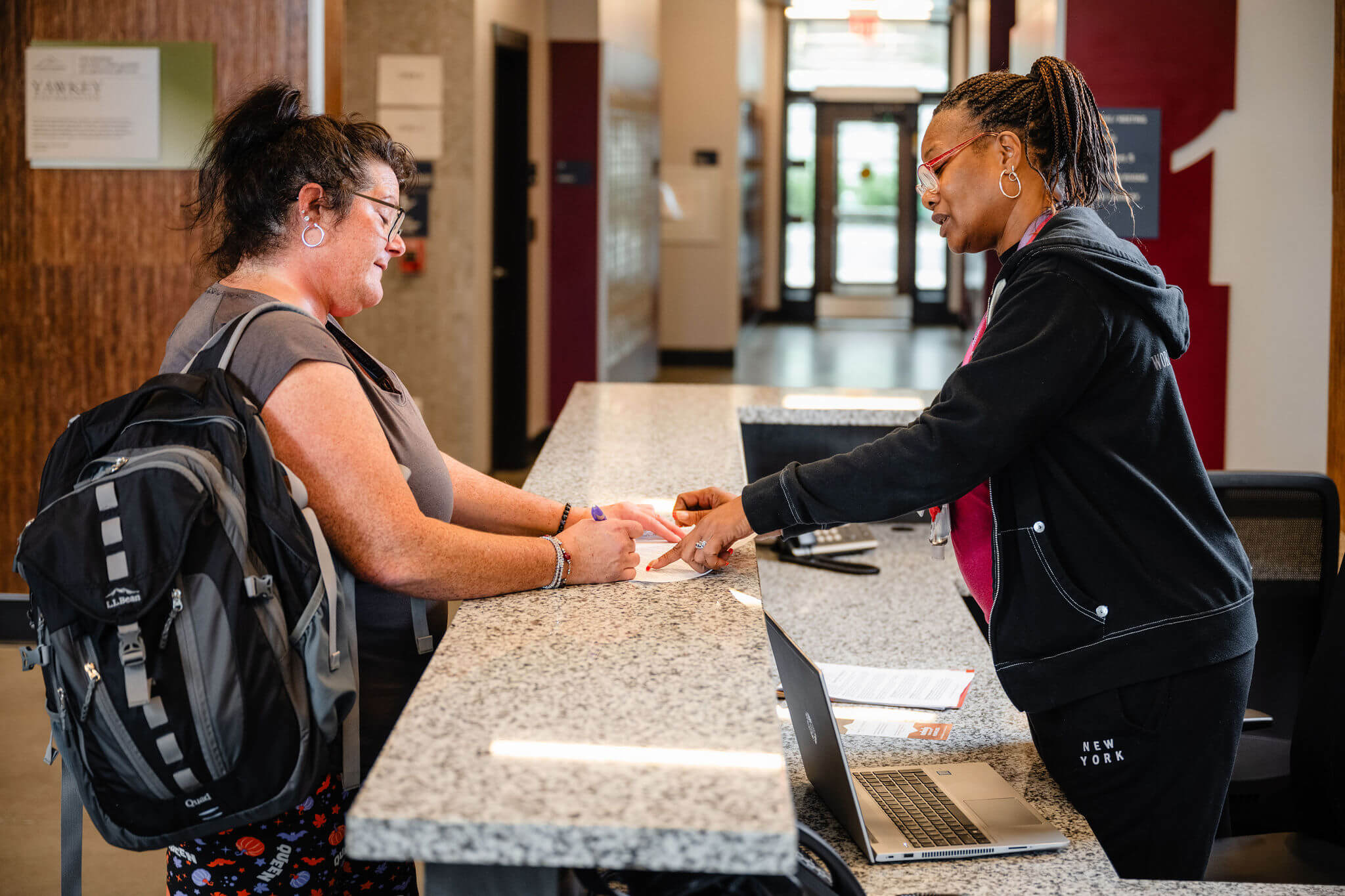 Two women standing at a counter signing paperwork.