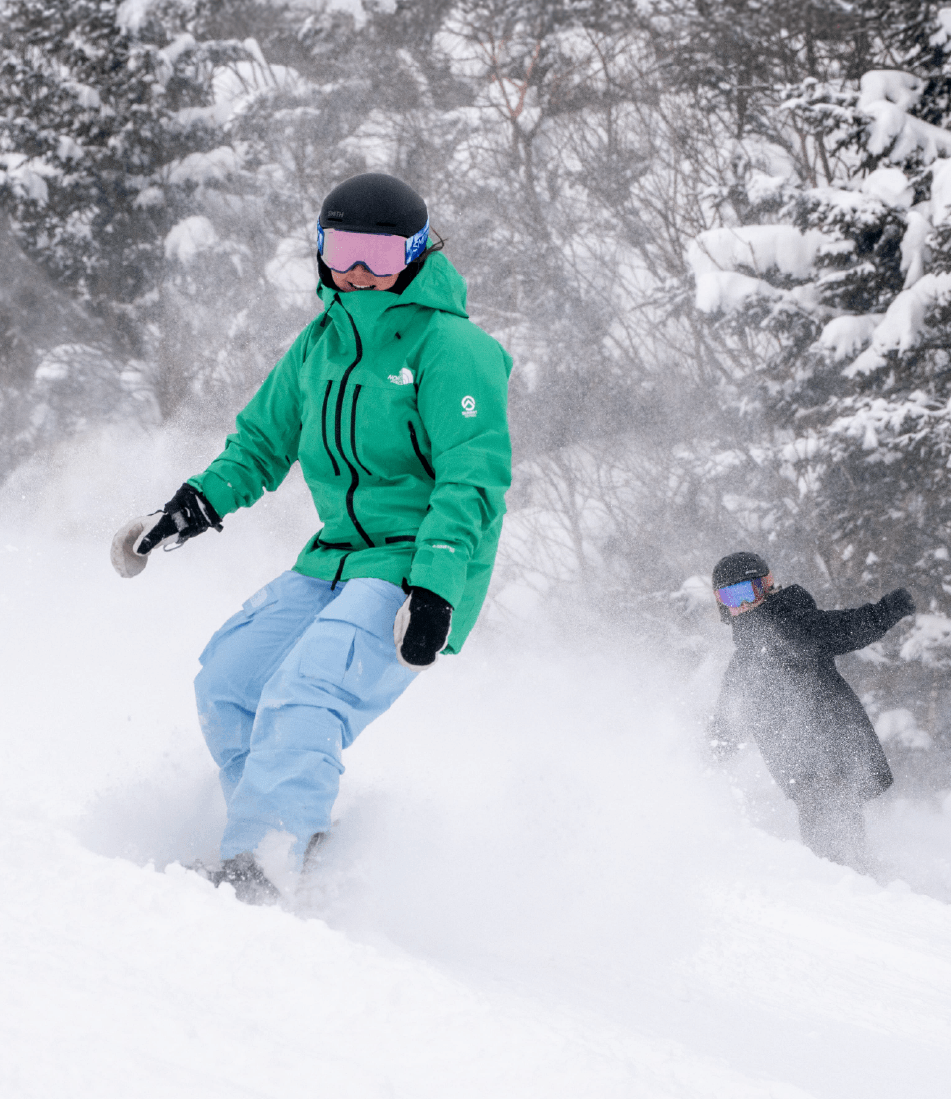 Three skiers, two adults and one child, carving down a groomed snowy slope under a bright blue sky.